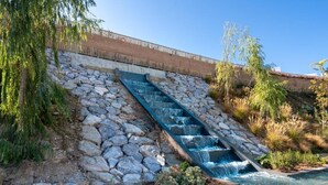A pool with a stone waterfall feature, surrounded by greenery and a stone retaining wall. - Casa Banderas - 2 BR (6p) - Pool view & mountains - La Cala De Mijas (Cala de Mijas)