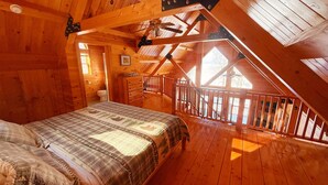 A wooden cabin bedroom with a bed, a bathroom, and a balcony with a wooden railing.