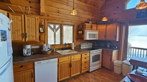 A wooden cabin-style kitchen with a refrigerator, microwave, stove, and wooden cabinets.