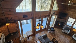 A cabin interior with a fireplace, wooden floors, and large windows.