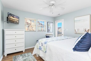 A bedroom with a bed, dresser, ceiling fan, and a TV mounted on the wall.