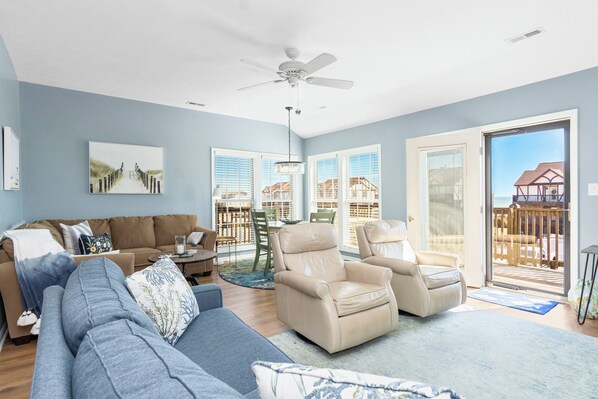 A living room with a sofa, armchairs, a ceiling fan, and a view of the outside.