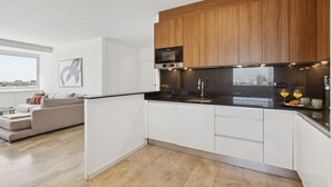 A modern kitchen with wooden cabinets, a black countertop, and a view of the city. - 2-Bed Apartment with Views of Plaza de Colón (Madrid)