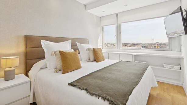 A modern bedroom with a large bed, a TV on the wall, and a city view. - 2-Bed Apartment with Views of Plaza de Colón (Madrid)