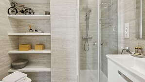 A modern bathroom with a glass-enclosed shower, white shelves with toiletries, and a bicycle decoration. - 2-Bed Apartment with Views of Plaza de Colón (Madrid)