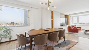 A modern dining area with a wooden table and chairs, a city view, a bookshelf, and a TV. - 2-Bed Apartment with Views of Plaza de Colón (Madrid)