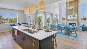 Une cuisine spacieuse dotée d’un grand îlot central, de luminaires suspendus modernes et d’un coin repas avec des chaises bleues et un tapis à rayures.