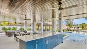 Un vaste espace extérieur aménagé en cuisine, avec un grand îlot central, des sièges et une piscine.