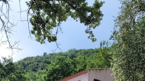Um edifício de dois andares com varanda, parede de pedra e entrada por caminho de cascalho.