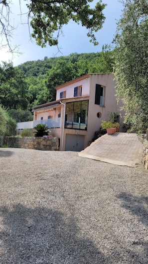 A two-story building with a balcony, a stone wall, and a gravel driveway.
