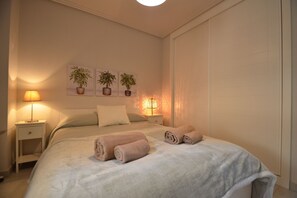 A bedroom with a bed, two bedside lamps, a nightstand, a wall-mounted plant, and a door. - Las Arenas 197 - Two Bedroom Apartment, Sleeps 5 (Punta del moral)