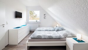 A bedroom with a bed, bedside table, and a TV mounted on the wall. - Vacation apartment "Tillmanns Pusteblume" in Norddeich - quiet & close to the beach (Norden)