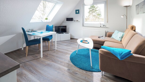 A modern, well-lit room with a dining table, chairs, a sofa, and a TV. - Vacation apartment "Tillmanns Pusteblume" in Norddeich - quiet & close to the beach (Norden)