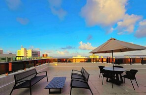 Una terraza en la azotea con una mesa, sillas, un banco y un paraguas grande.