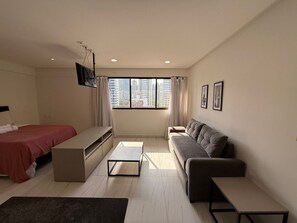 Una habitación moderna y bien iluminada con cama, sofá y televisor montado en la pared.