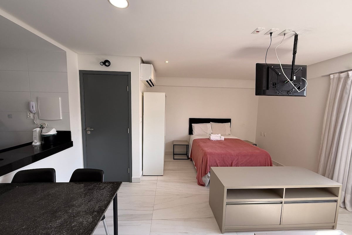 Una habitación de hotel moderna con una cama, un escritorio, una silla, un televisor montado en la pared y una puerta.