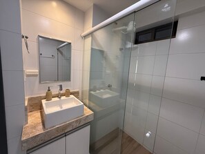Un baño moderno con ducha de vidrio, un lavabo blanco con dos grifos y un espejo sobre el lavabo.