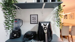 Une petite cuisine équipée d’une machine à café, d’un mixeur et d’une bouilloire, le tout placé sur une étagère, et entouré de plantes vertes.