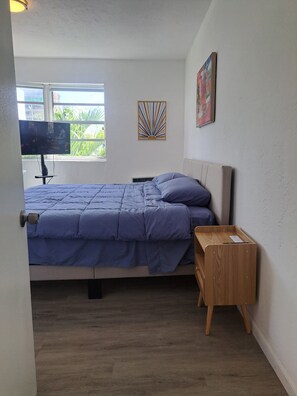 A bedroom with a bed, a TV, a window, and a wooden nightstand. - Phenomenal Studio - Steps to Beach - Great Views - Historic - terrific stay (Surfside)