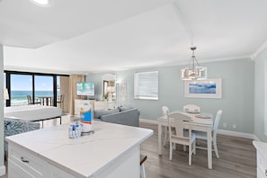 A modern living room with a large window, a dining area, and a kitchen island.