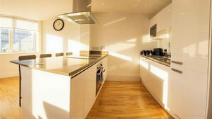 A modern kitchen with a central island, wooden flooring, white cabinetry, and a large window providing natural light. - Greenwich Apartment Near Cutty Sark and Paid Parking (London)