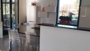 Une cuisine moderne avec un coin repas, des chaises transparentes et une vue sur l’extérieur.