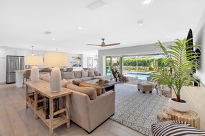 A modern living room with a sofa, coffee table, and a dining area with a chandelier. - VRCC Villa Cozy Cape (Cape Coral)