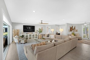 A spacious living room with a sectional sofa, a TV, and a ceiling fan. - VRCC Villa Cozy Cape (Cape Coral)