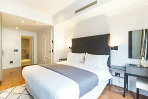 Ett hotellrum med en stor säng, ett skrivbord med en stol, en spegel och en dörr som leder till ett badrum.