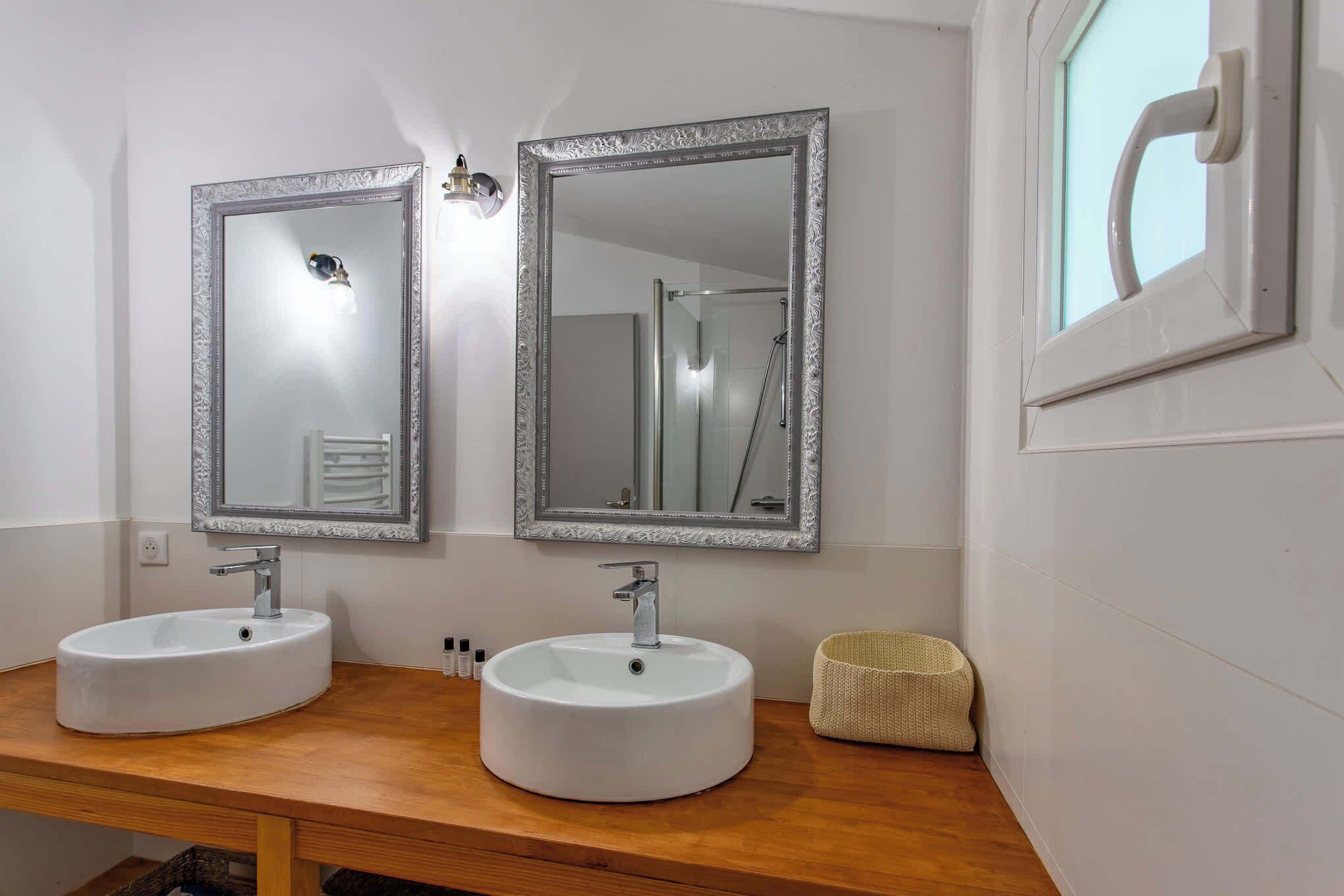 Een badkamer met twee wasbakken, elk met een spiegel erboven. Een douche is zichtbaar op de achtergrond.
