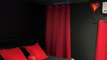 A bed with red pillows, a heart-shaped balloon, and rose petals on the floor.
