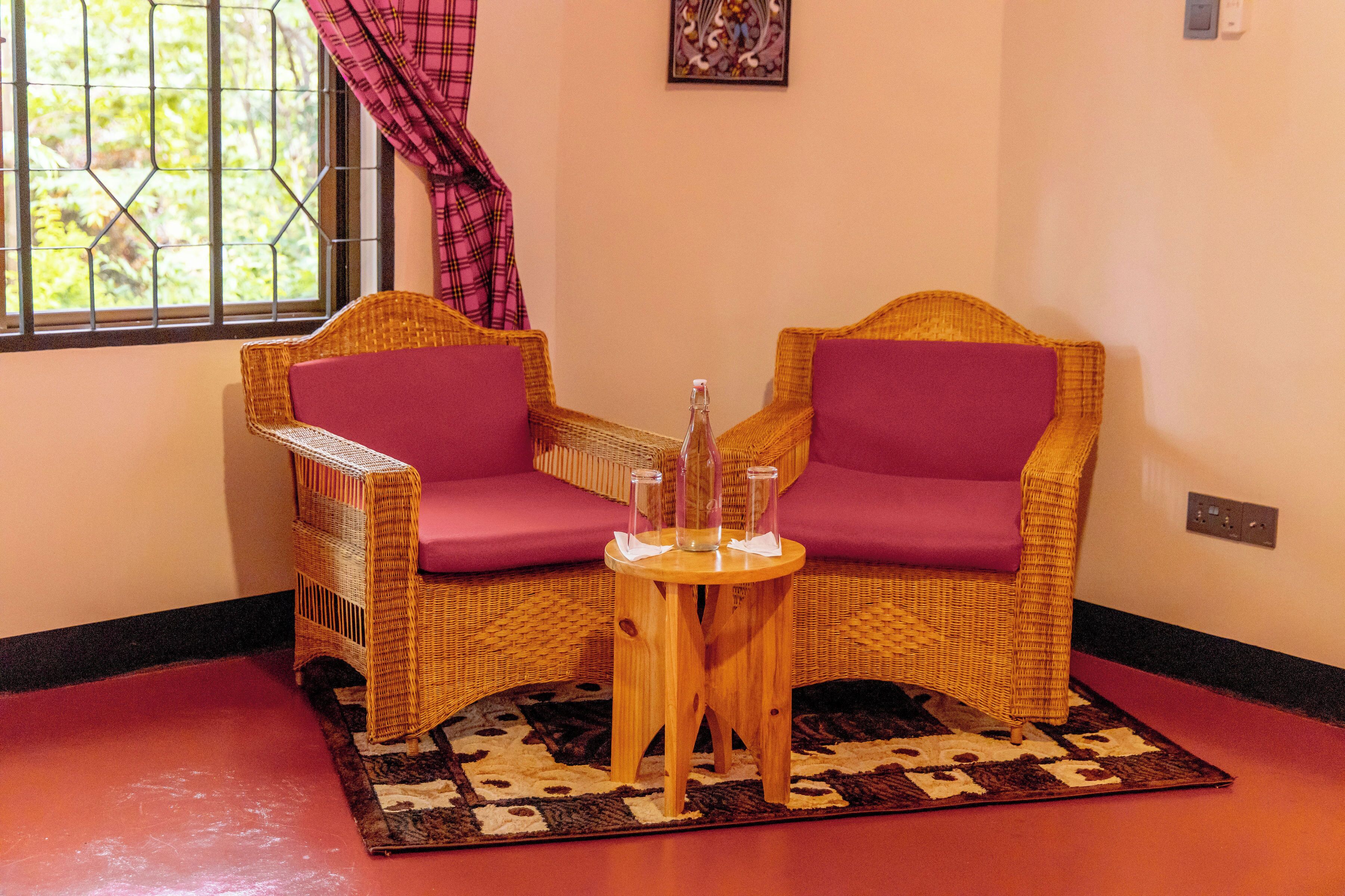 Habitación de esquina con sillones de mimbre, una mesita de madera y un tapete estampado.
