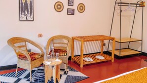 Une pièce avec des chaises en osier, une petite table en bois, un porte-chaussures suspendu et des œuvres d’art murales.