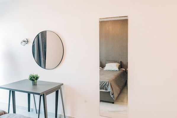 Um quarto com um espelho redondo, uma mesinha com uma planta e uma cama com cabeceira listrada.
