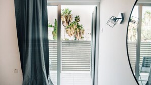Quarto com porta de vidro deslizante que dá para uma varanda com palmeiras e guarda-corrimão branco.