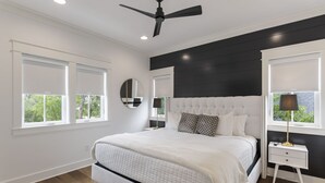 Una camera da letto con un letto grande, un ventilatore a soffitto, un comodino con una lampada e una finestra vista verde.