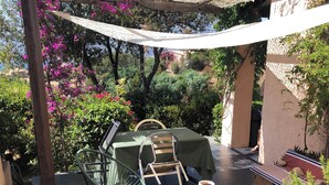 En udendørs terrasse med grill, stole og borde under et pergolaoverdækning.