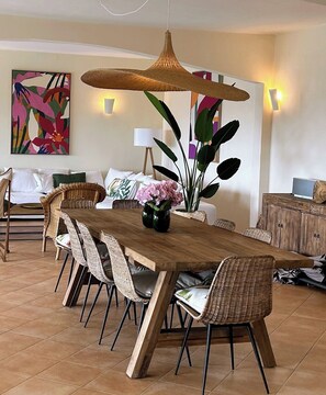 A dining area with a long wooden table, wicker chairs, a dining accessories, and a hanging light fixture. - Villa with breathtaking view of the Gulf of St-Tropez 5 mins from the sea and shops (Roquebrune-sur-Argens)