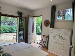 A bedroom with a bed, a dresser, a chair, and a door leading to a garden. - Villa with breathtaking view of the Gulf of St-Tropez 5 mins from the sea and shops (Roquebrune-sur-Argens)