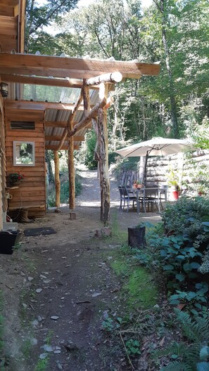 A rustic wooden cabin with a covered porch, a dining area with outdoor seating, and a dirt path leading to the cabin. - Chalet-style house tucked away in the woods (Lespinassière)
