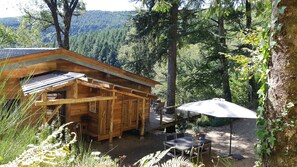 A wooden cabin with a deck, outdoor seating, and a view of a forested hillside. - Chalet-style house tucked away in the woods (Lespinassière)
