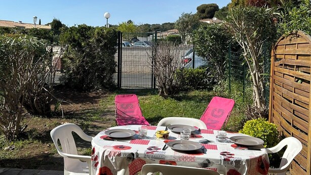 Eine Terrasse im Freien mit Esstisch, umgeben von Pflanzen und einem Zaun.