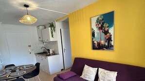 Ein kompakter Wohnbereich mit Essplatz, Küchenzeile und einem violetten Sofa mit Kissen.