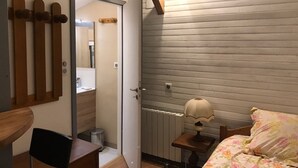 Makuuhuoneessa on sänky, yöpöytä, lamppu, patteri ja ovi, joka johtaa kylpyhuoneeseen.