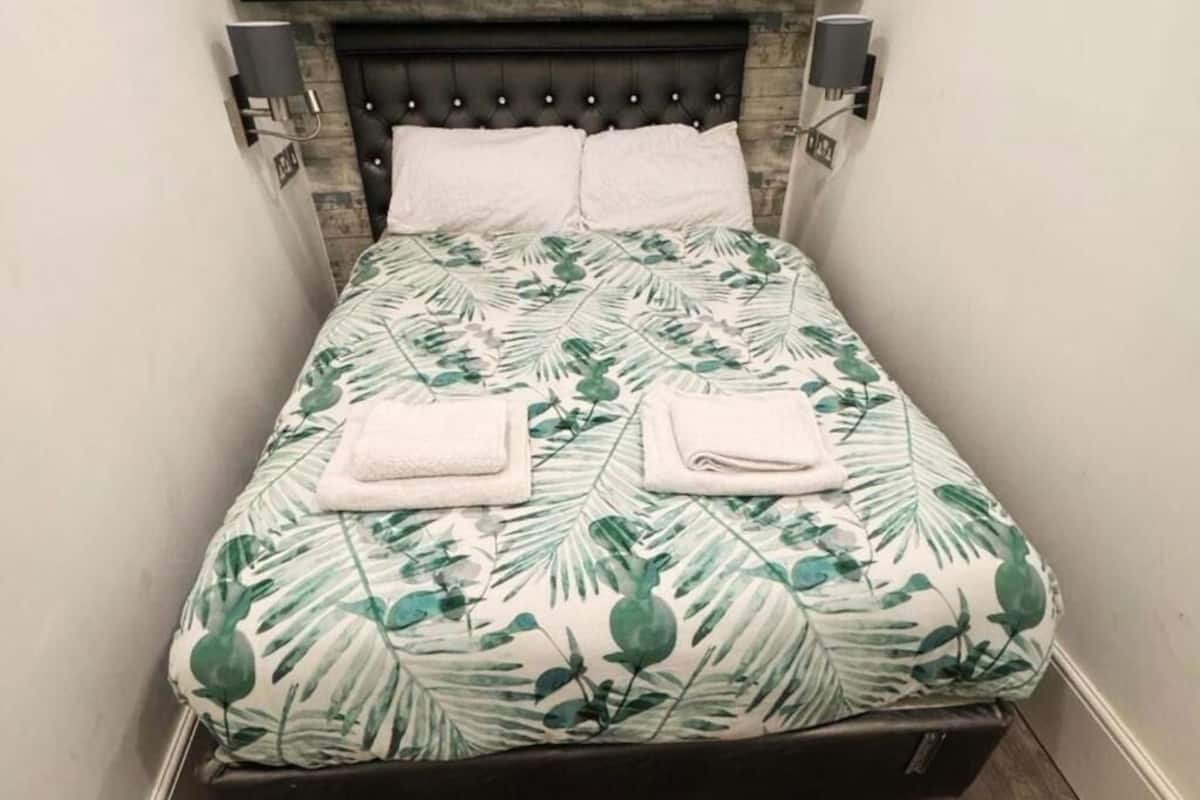 Un lit avec une couvre-lit à motifs de feuilles, deux oreillers et deux serviettes pliées.