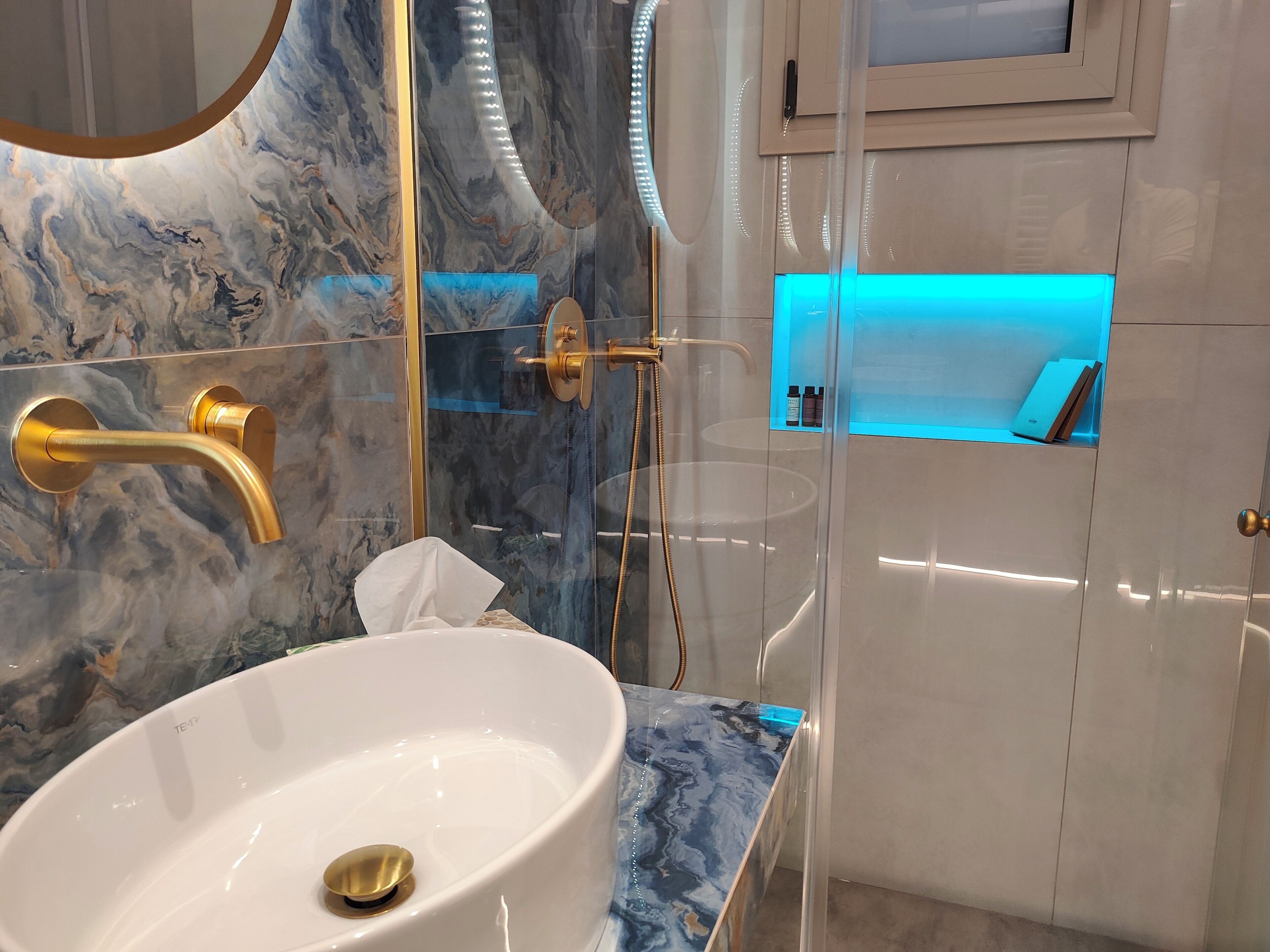 A bathroom with a marble sink, gold fixtures, and a glass-enclosed shower area.