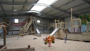 Ein Indoor-Spielbereich mit Rutschen, einer Kletterlandschaft und einem Sandkasten.