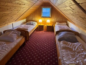 Ein kleines Schlafzimmer im Dachgeschoss mit zwei Holzbettgestellen, einem roten Teppich mit Blumenmuster und einem Oberlicht.