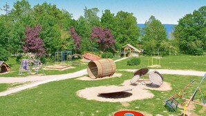 Ein Spielplatz mit verschiedenen Spielgeräten, einer kleinen Laube und einem Weg zu einem Gewässer.