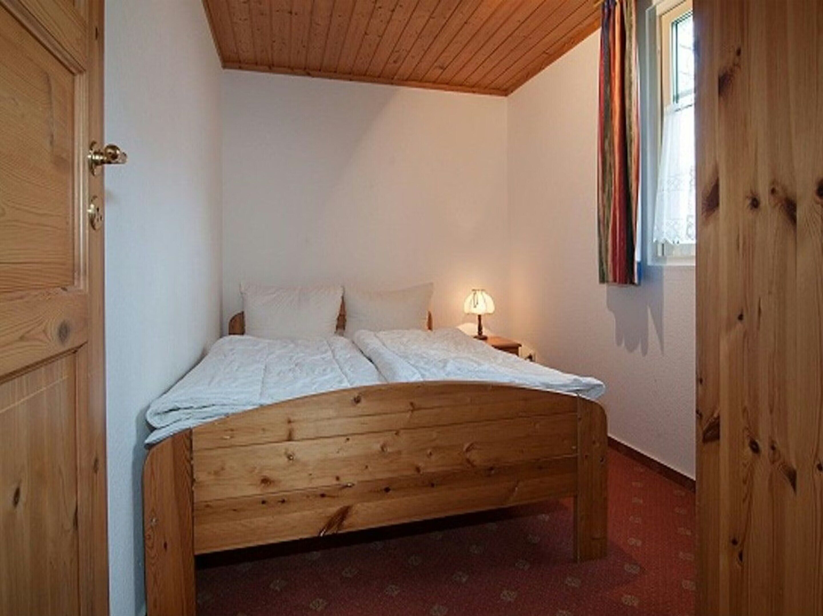 A wooden bed in a room with a sloped ceiling and a window with curtains.
